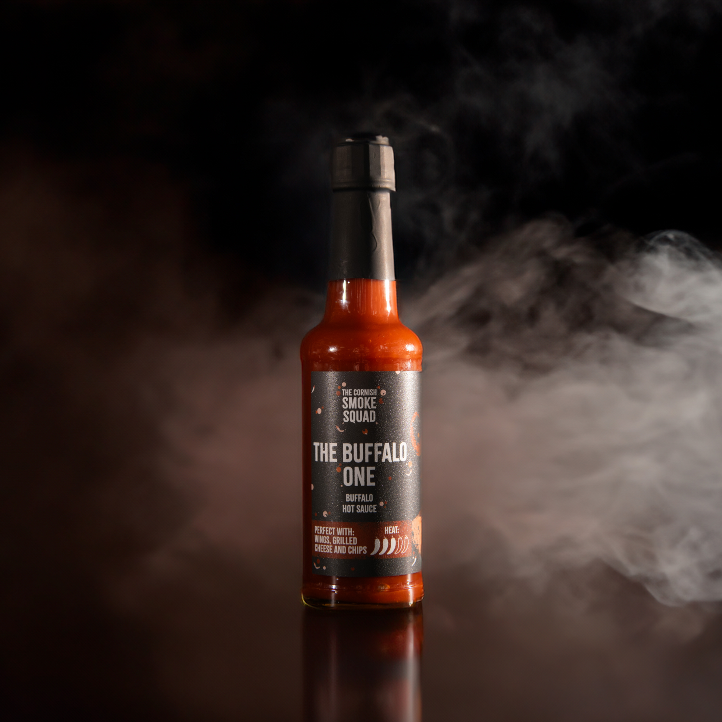 Buffalo hot sauce from the cornish smoke squad in front of a black background with white and brown smoke around it
