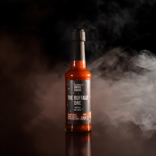 Buffalo hot sauce from the cornish smoke squad in front of a black background with white and brown smoke around it