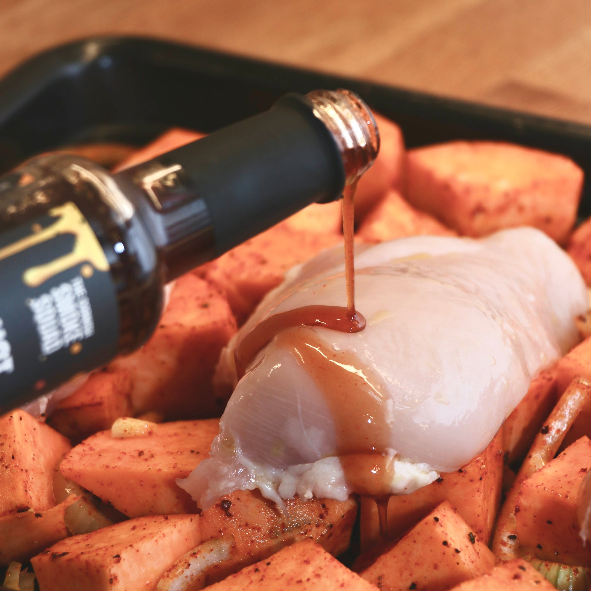 Bottle of sauce being poured over chicken breast
